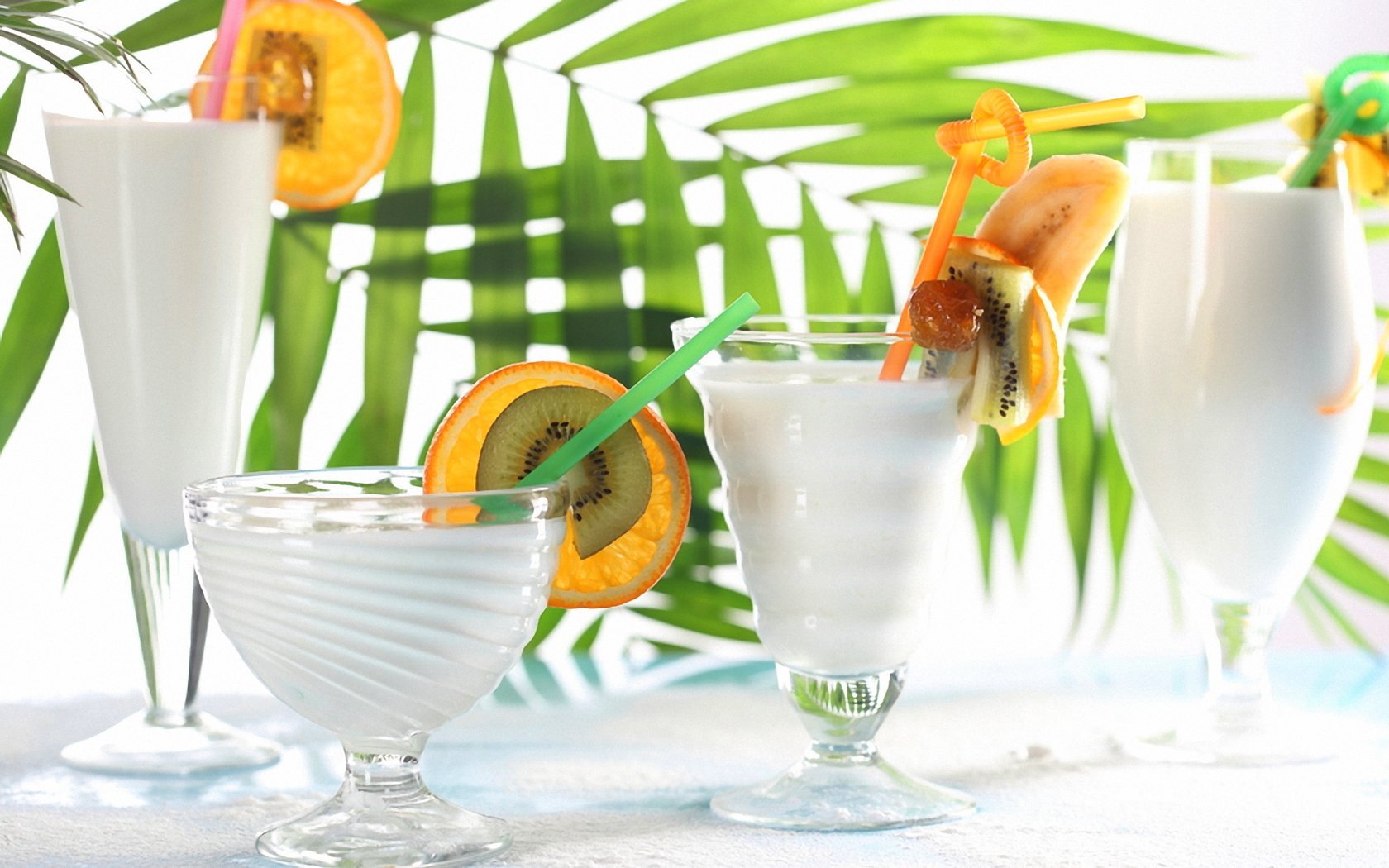 HD PC desktop wallpaper featuring a refreshing assortment of white cocktails garnished with citrus slices against a vibrant green palm leaf background.