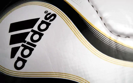 Close-up of an Adidas logo on a textured surface, showcasing the brand's iconic design in black and white with gold accents. A striking HD desktop wallpaper background.