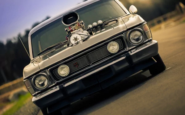 HD desktop wallpaper featuring a close-up front view of a customized Ford Cortina with a powerful engine exposed through the hood, set against a blurred outdoor background.