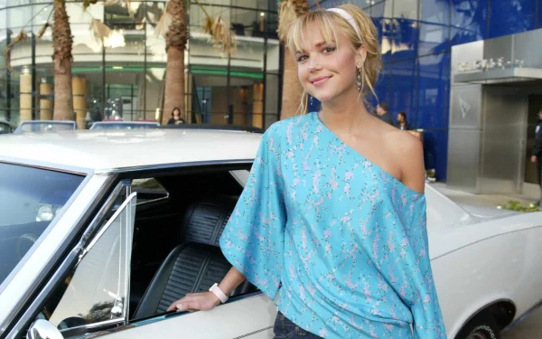 HD wallpaper of a woman in a blue one-shoulder top, standing next to a white car in an outdoor setting, tagged with Arielle Kebbel.