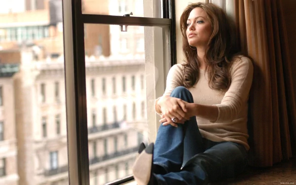 HD desktop wallpaper of celebrity Angelina Jolie sitting by a window, looking thoughtfully outside.
