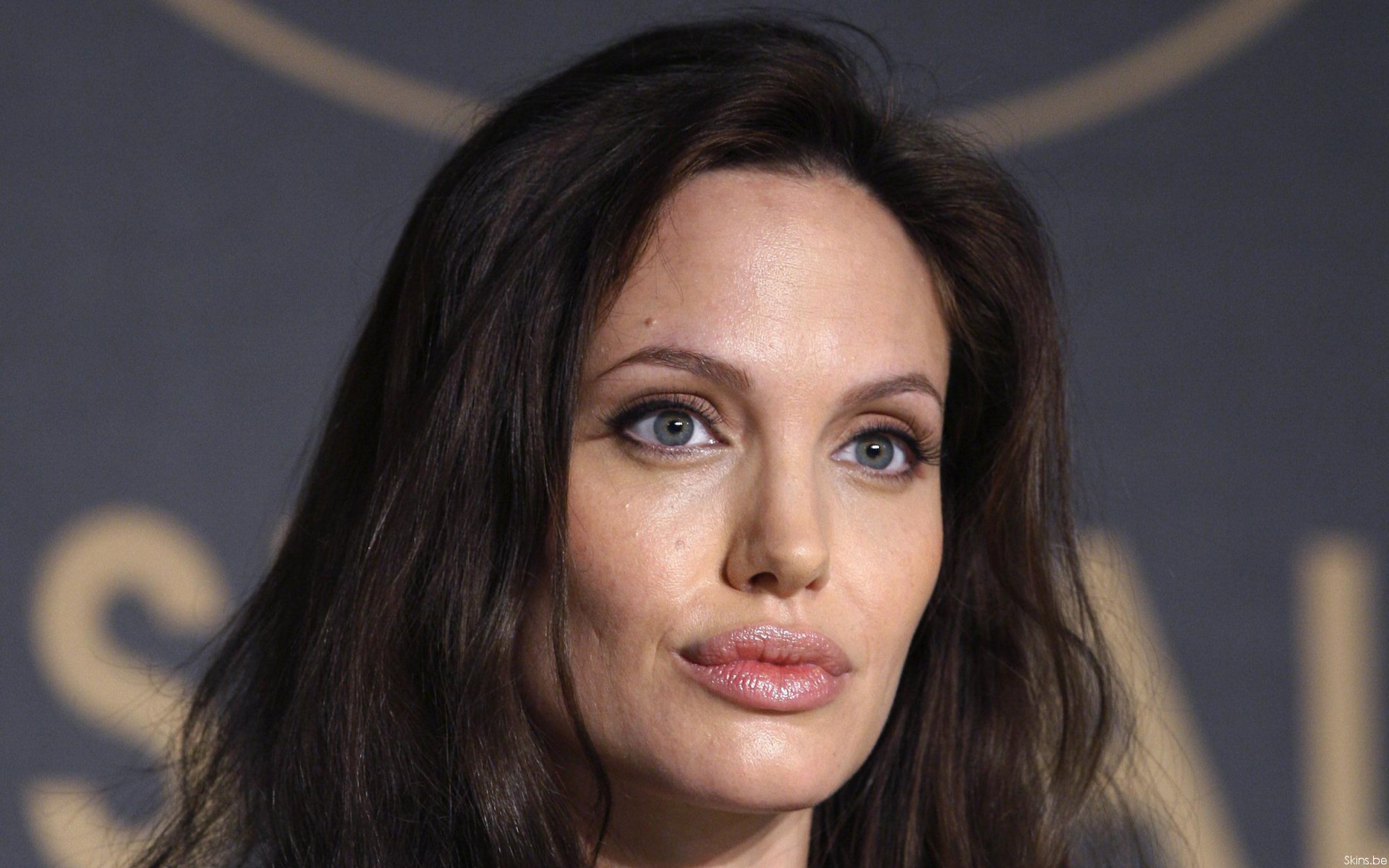 HD PC desktop wallpaper featuring a close-up portrait of celebrity Angelina Jolie with natural makeup and flowing dark hair against a blurred background.