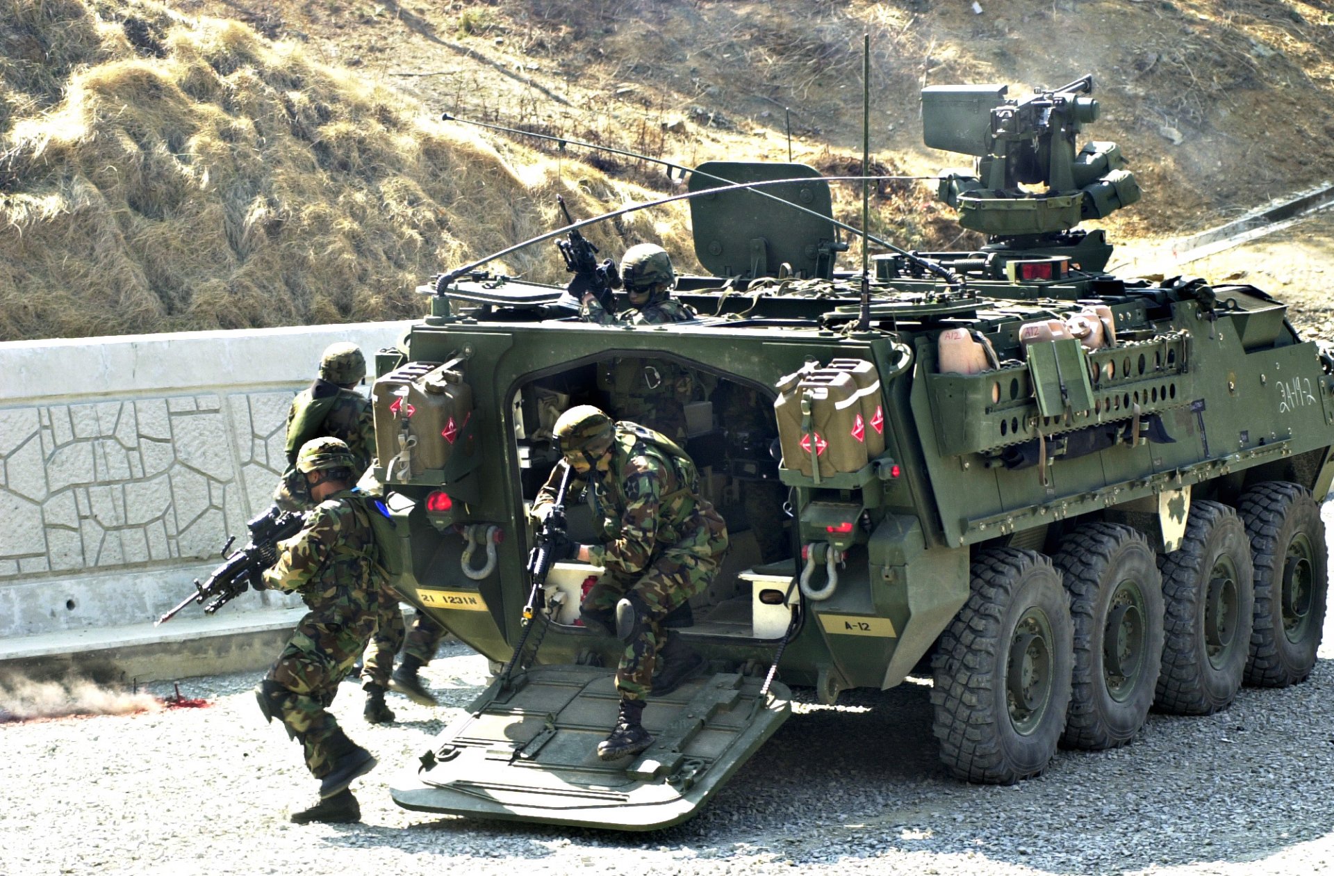 HD PC desktop wallpaper depicting a military vehicle with soldiers in camouflage gear loading into the armored transport on a rugged terrain.