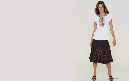 Unidentified woman in a white embroidered top and black skirt standing against a pale background — HD PC desktop wallpaper and background.