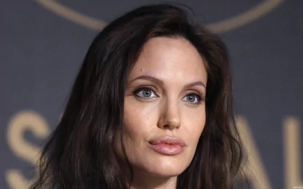 HD PC desktop wallpaper featuring a close-up portrait of celebrity Angelina Jolie with natural makeup and flowing dark hair against a blurred background.