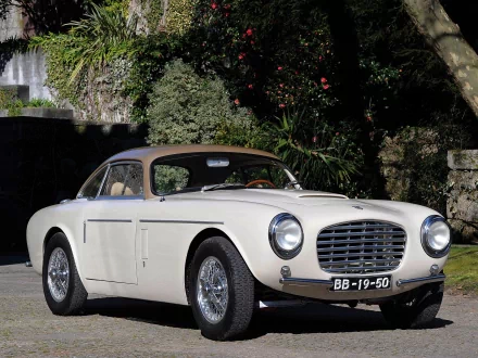 HD PC desktop wallpaper of a white Siata vehicle parked by a stone wall and lush garden, front three-quarter view showcasing chrome grille, round headlights and wire-spoke wheels.