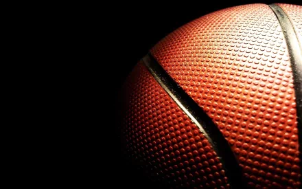 Close-up of a textured basketball against a dark background, showcasing its surface details. An energetic and dynamic wallpaper for basketball and sports enthusiasts.
