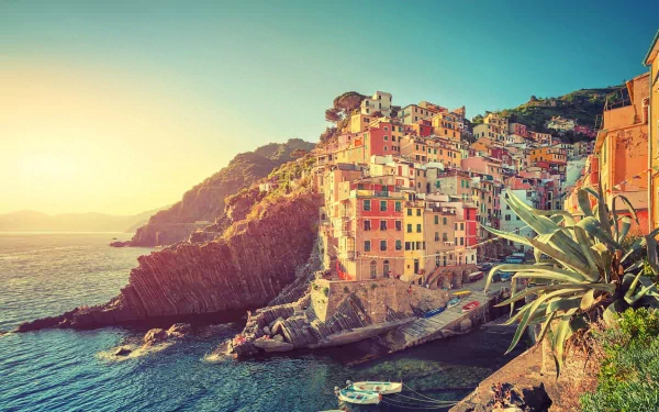 Scenic view of Riomaggiore in Cinque Terre, showcasing colorful man-made buildings on rugged cliffs beside the sparkling sea, under a warm sunset sky.