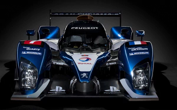 High-definition PC desktop wallpaper background featuring a blue Peugeot racing prototype vehicle shown head-on, with illuminated headlights and sleek aerodynamic bodywork.
