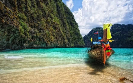 HD desktop wallpaper of a boat anchored in a turquoise lagoon, surrounded by towering cliffs under a partly cloudy sky.