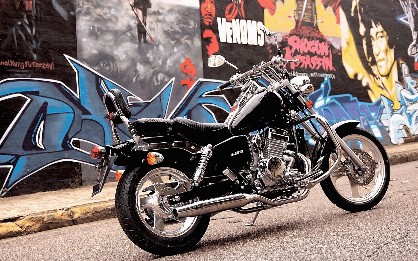 HD PC desktop wallpaper featuring a black motorcycle parked on a street with vibrant graffiti art on the wall behind it.