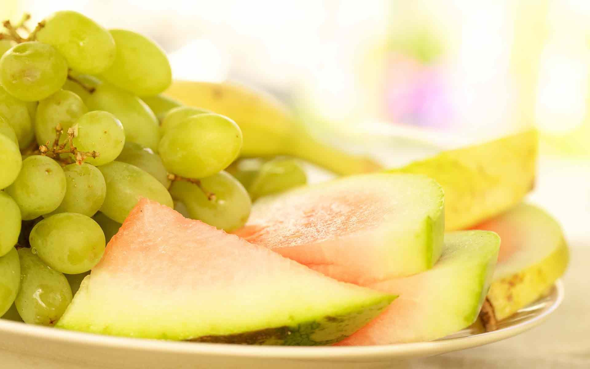 HD PC desktop wallpaper featuring a close-up of fresh green grapes, watermelon slices, and bananas, highlighting vibrant and healthy fruit in soft natural light.