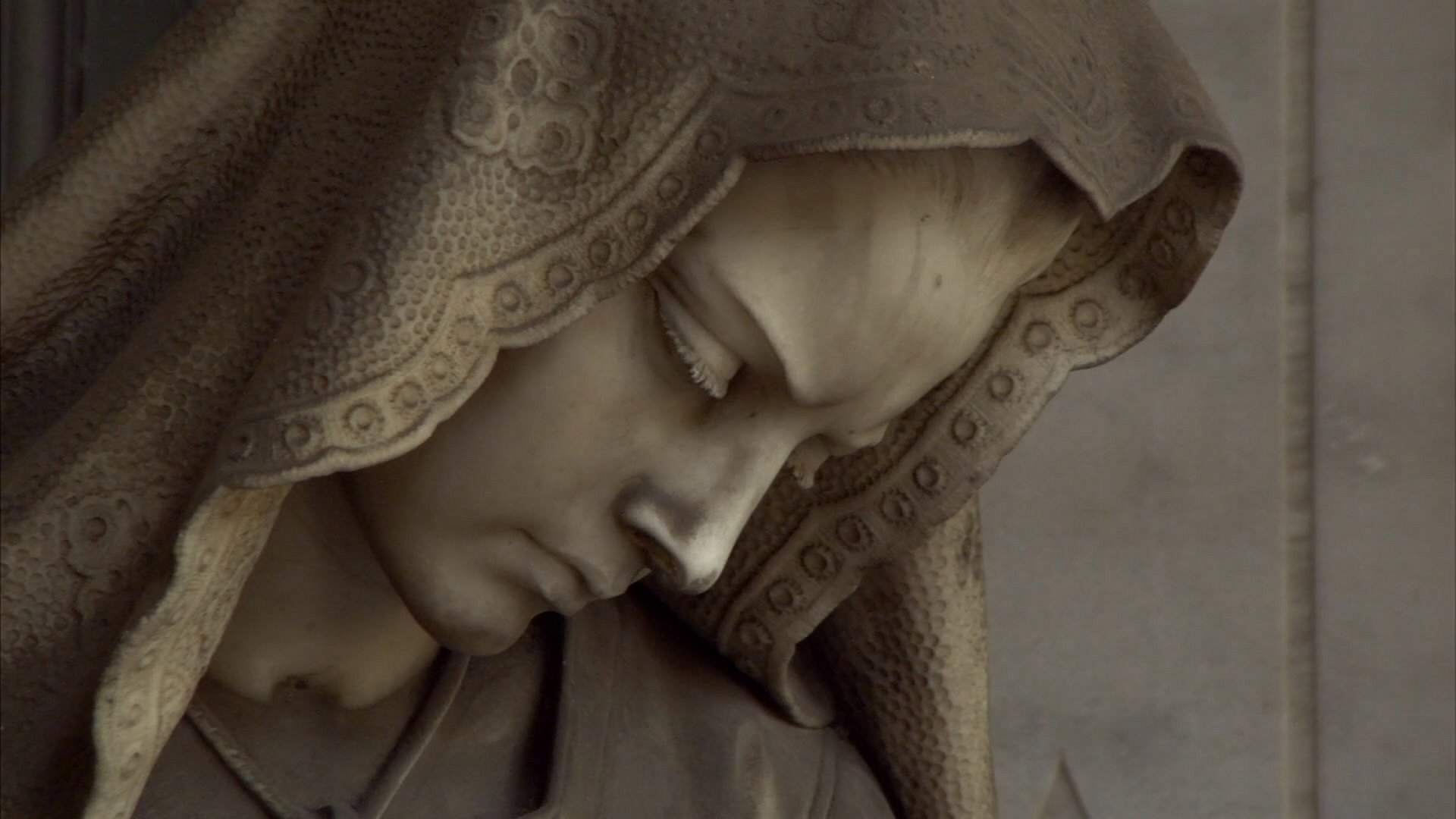 HD desktop wallpaper featuring a close-up of a man-made statue depicting a solemn, hooded figure with intricate carved details.