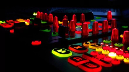 A vibrant HD desktop wallpaper showcasing a DJ's equipment, featuring illuminated buttons and controls in bold colors, capturing the dynamic essence of music and mixing.