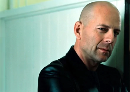 A striking HD desktop wallpaper featuring celebrity Bruce Willis. He leans casually against a wall, exuding confidence and a cool demeanor.