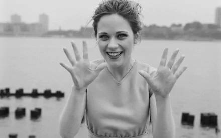 Black-and-white HD desktop wallpaper featuring celebrity Zooey Deschanel smiling with hands raised against a blurred outdoor waterfront background.