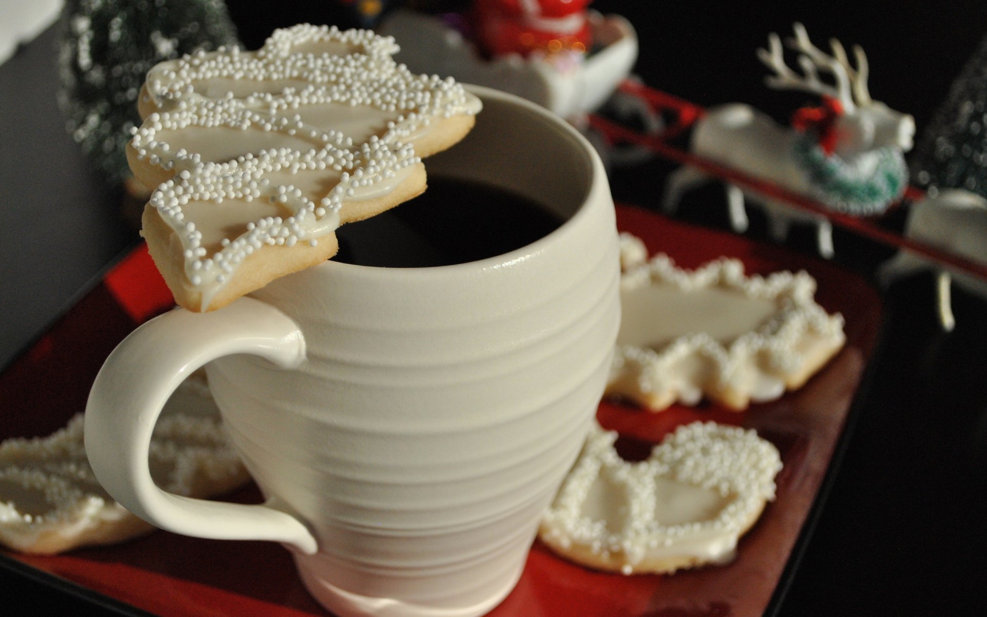 HD PC desktop wallpaper featuring a white mug with a Christmas tree-shaped cookie topped with white sprinkles, alongside festive sweets on a red and black background.