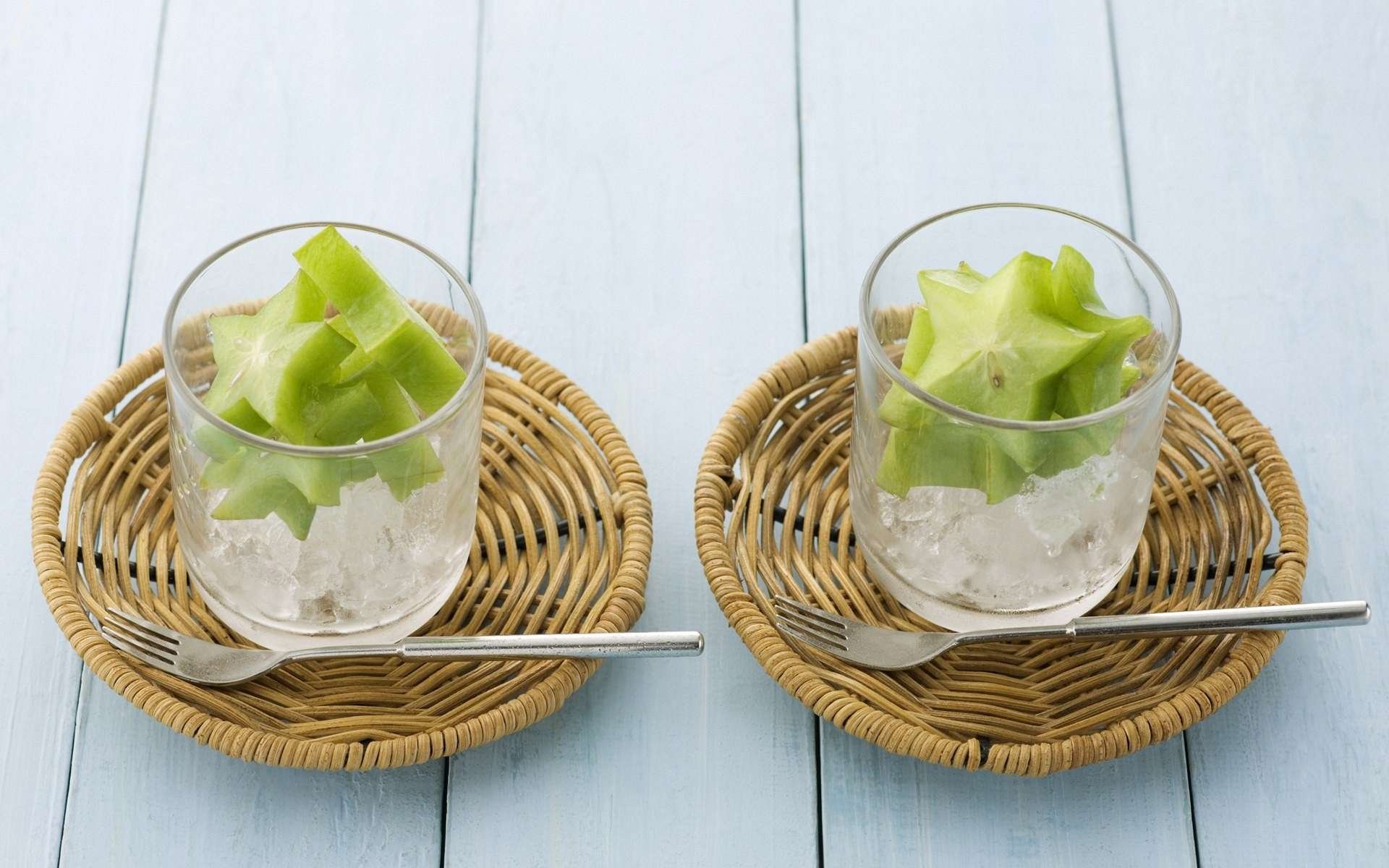 HD desktop wallpaper featuring two glasses filled with ice and fresh starfruit slices, each placed on a round wicker coaster with a metal spoon alongside.
