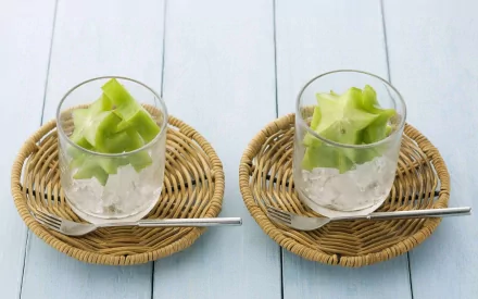 HD desktop wallpaper featuring two glasses filled with ice and fresh starfruit slices, each placed on a round wicker coaster with a metal spoon alongside.