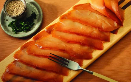 HD PC desktop wallpaper featuring a close-up of sliced smoked salmon on a wooden platter with herbs and sesame seeds on the side, highlighting a fresh meal presentation.