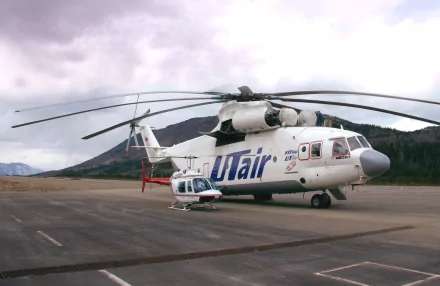 HD desktop wallpaper featuring a Mil Mi-26 helicopter with Utair livery on a tarmac surrounded by mountainous terrain under a cloudy sky.