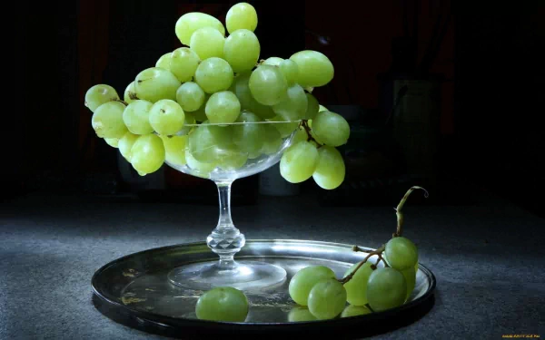 A stunning HD desktop wallpaper featuring a crystal glass filled with fresh green grapes, elegantly displayed on a silver tray against a dark background.