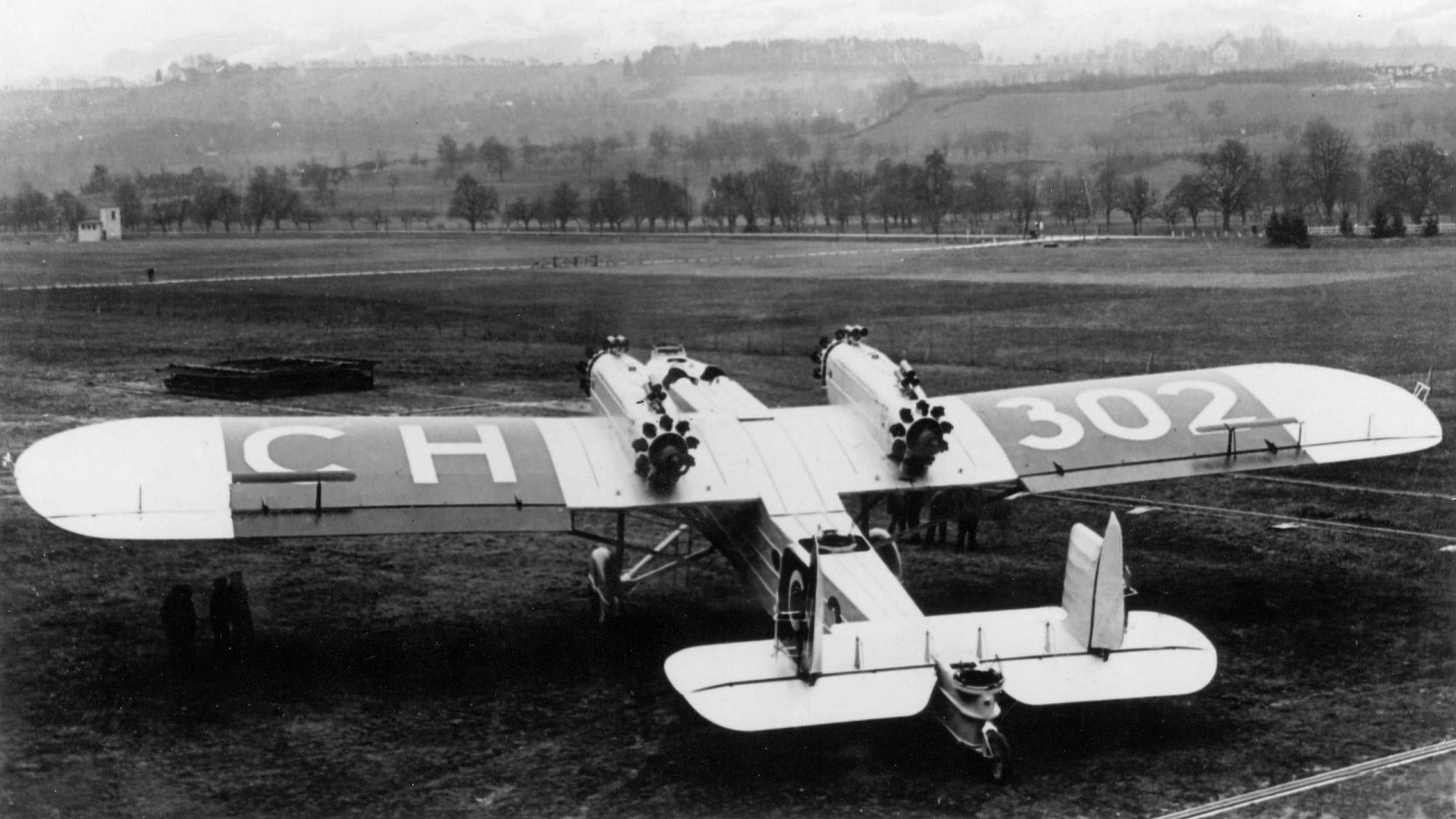 Black and white HD PC desktop wallpaper of a vintage multi-engine aircraft on a grassy airfield, showcasing classic airplane design and early aviation history.