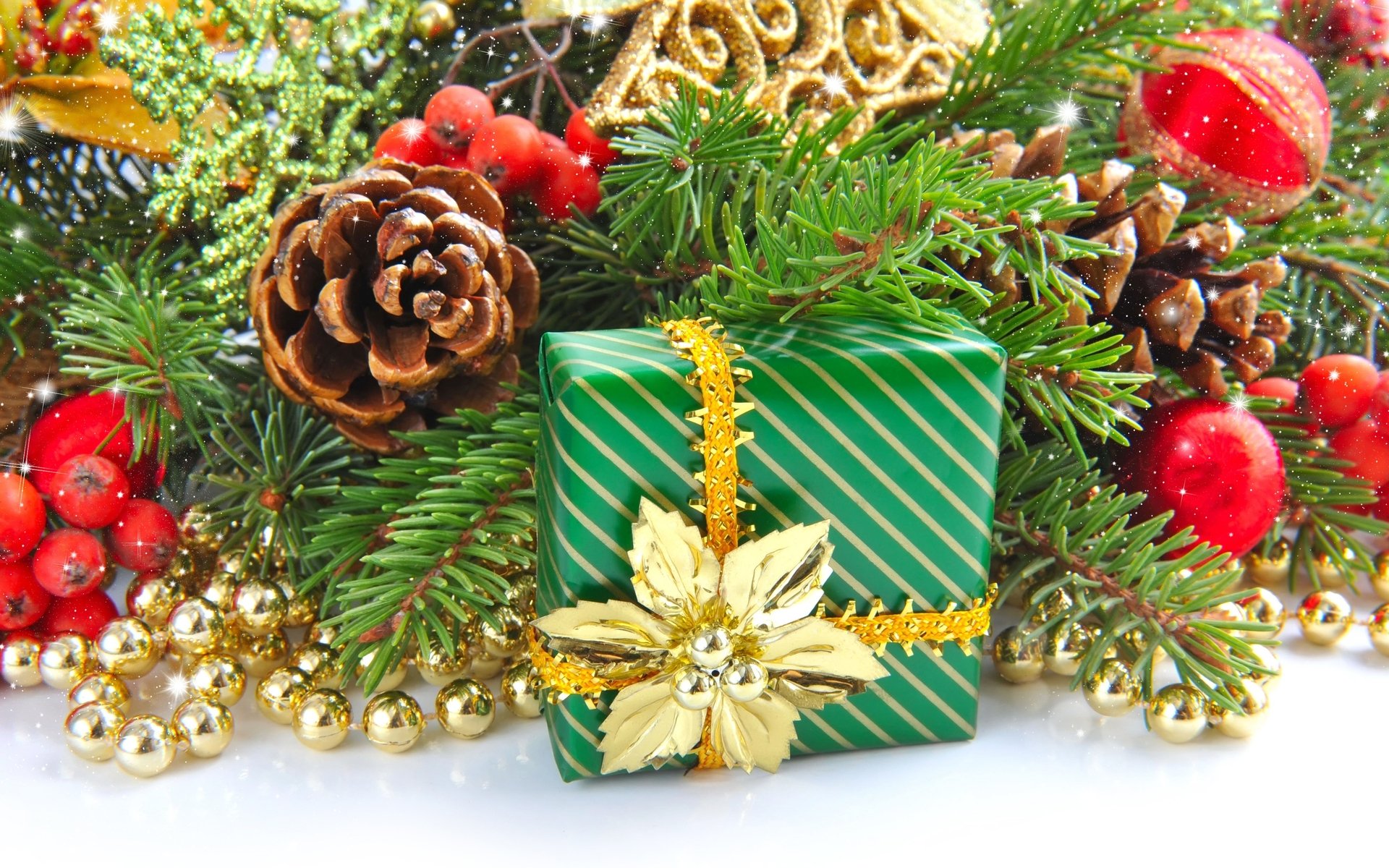 A beautifully wrapped green Christmas gift surrounded by festive ornaments, pine cones, and holiday greenery, creating a cheerful holiday atmosphere. HD wallpaper for desktop use.