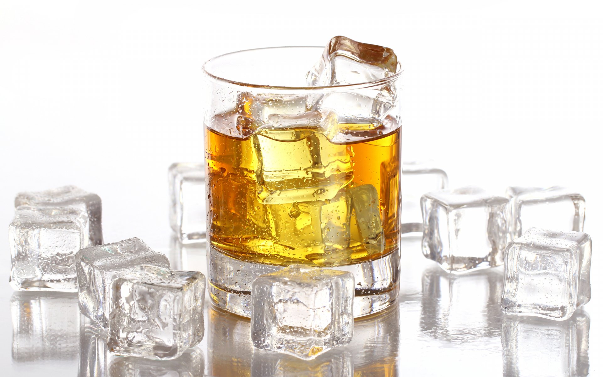 HD desktop wallpaper featuring a glass of whisky with ice cubes, surrounded by extra ice on a reflective surface, highlighting the rich amber color of the drink.