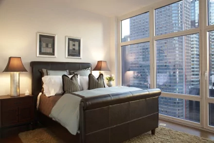 4K Ultra HD PC desktop wallpaper/background: man-made modern bedroom with leather bed, pillows and lamps, floor-to-ceiling windows revealing city skyscrapers.
