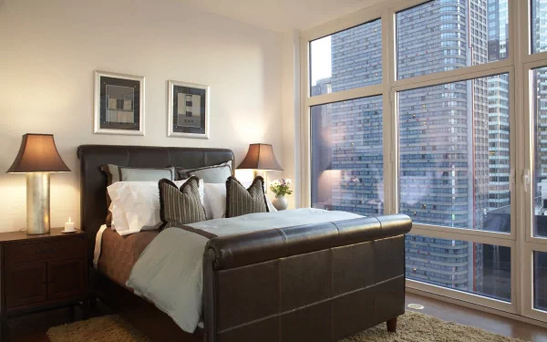 4K Ultra HD PC desktop wallpaper/background: man-made modern bedroom with leather bed, pillows and lamps, floor-to-ceiling windows revealing city skyscrapers.