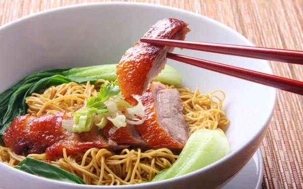 HD PC desktop wallpaper featuring a bowl of noodles with roasted meat, green vegetables, and chopsticks holding a piece of meat, highlighting a delicious meal.