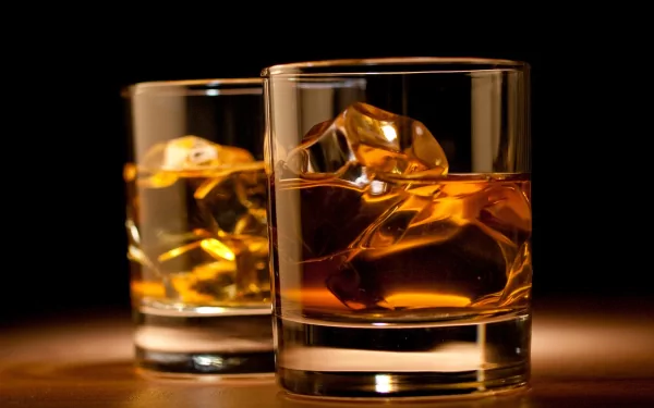 Two glasses of whisky on a dark background, featuring ice cubes and showcasing golden hues. A refined food and drink-themed HD desktop wallpaper.