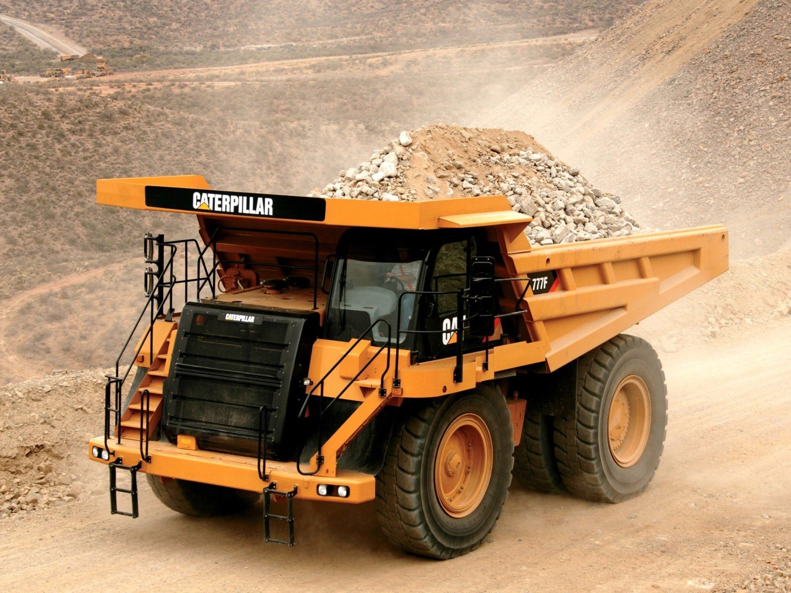 HD desktop wallpaper featuring a Caterpillar Inc. heavy-duty mining dump truck on a dusty construction site.