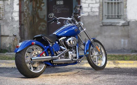 A blue Harley-Davidson motorcycle is parked in front of a weathered brick building. This image serves as an HD desktop wallpaper and background.