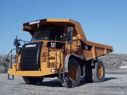 HD desktop wallpaper featuring a large Caterpillar Inc. heavy-duty dump truck vehicle against a clear blue sky and gravel background.