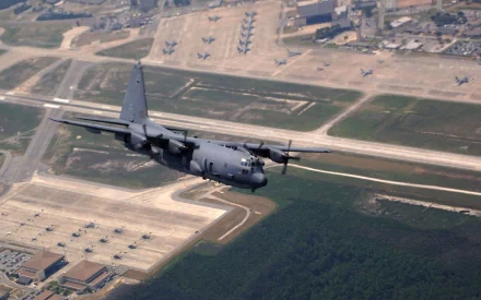 A Lockheed AC-130 military aircraft flies over an airbase in this HD desktop wallpaper and background image.