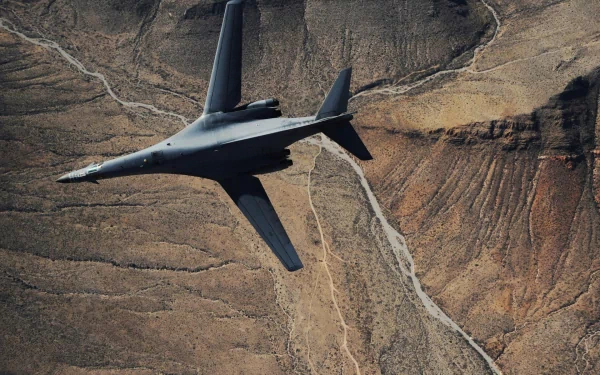 A Rockwell B-1 Lancer military bomber flying over a rugged desert landscape, captured in an HD PC desktop wallpaper and background.