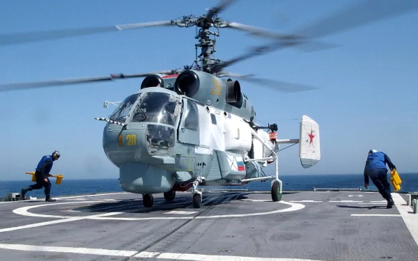 A Kamov Ka-27 military helicopter takes off from a ship's deck, with crew members preparing for flight against a clear blue sky, creating a dynamic HD desktop wallpaper.