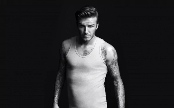 David Beckham poses confidently in a black and white image, showcasing his tattoos. This striking visual serves as an engaging HD desktop wallpaper for sports enthusiasts.