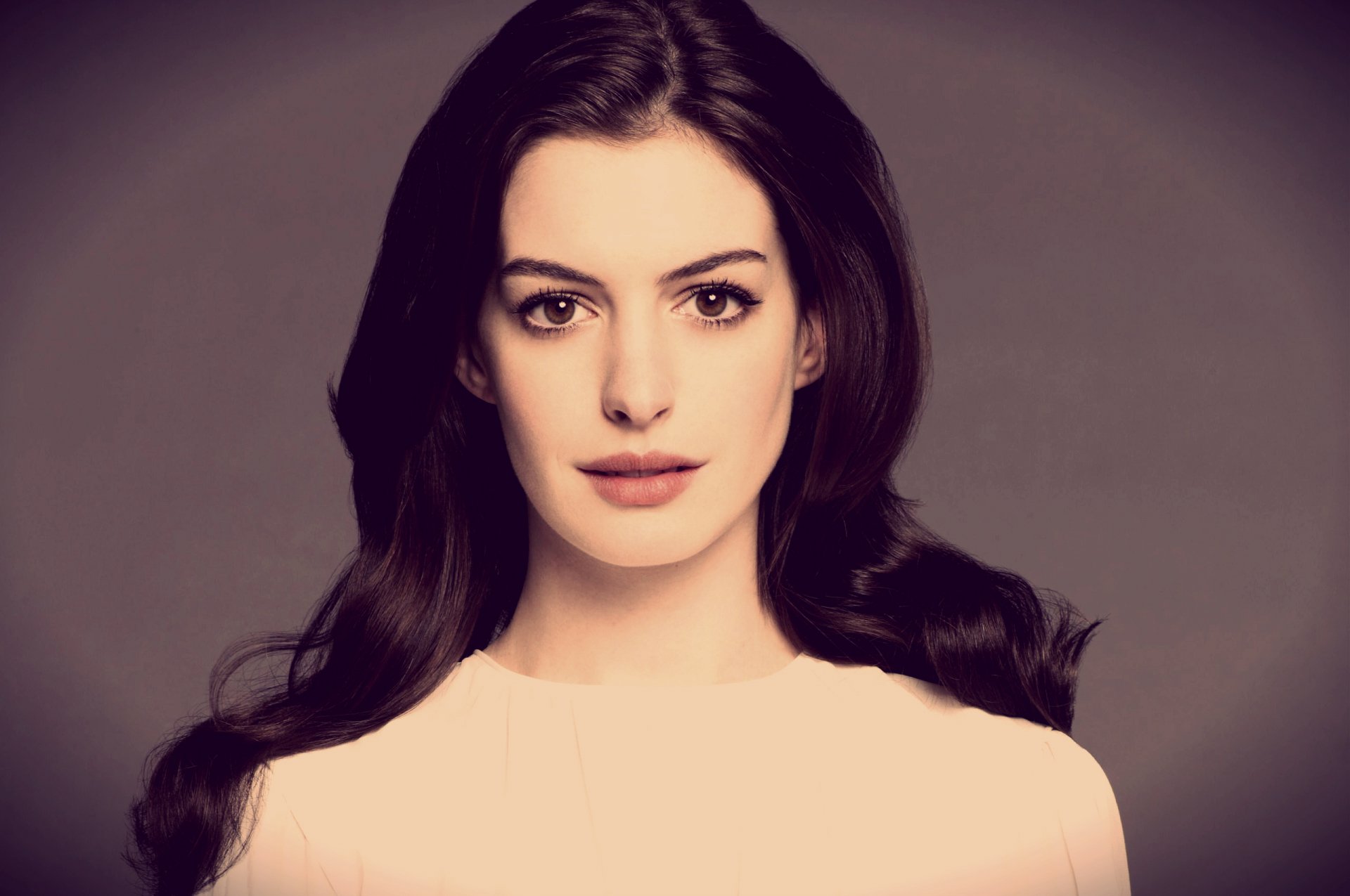 A high-definition desktop wallpaper featuring Anne Hathaway, showcasing her with long, dark hair and a neutral expression against a soft background.