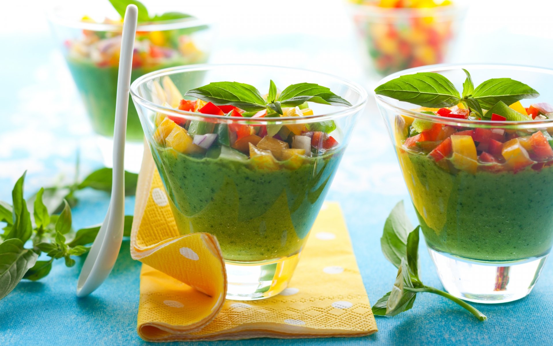 HD PC desktop wallpaper of vibrant green smoothies garnished with fresh basil and colorful diced vegetables in clear glass cups on a blue surface.