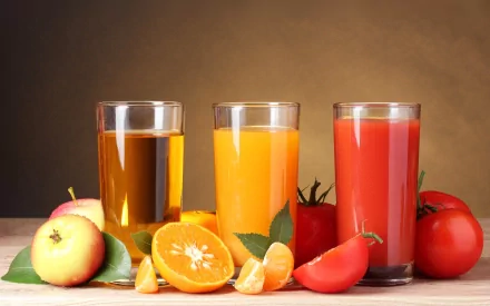 HD PC desktop wallpaper featuring three glasses of juice—apple, orange, and tomato—surrounded by fresh fruits and tomatoes on a neutral background.