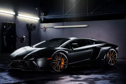 A sleek black Lamborghini Aventador is showcased in a dimly lit garage, featuring striking orange wheel details, creating a dramatic and captivating HD desktop wallpaper.