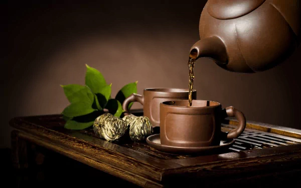 A serene moment featuring a teapot gracefully pouring tea into two clay cups, surrounded by green leaves and tea buds, set against a warm, soothing background. 4K Ultra HD wallpaper.