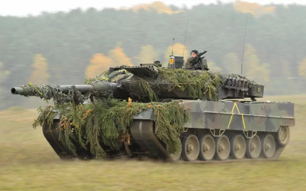 A soldier stands atop a camouflaged Leopard 2 tank, moving through a landscape lush with greenery, embodying military strength and strategy. HD wallpaper showcasing military prowess.