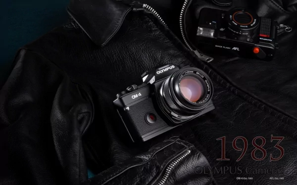 HD desktop wallpaper featuring an old Olympus OM-4 camera with a vintage lens resting on a black leather jacket, showcasing classic man-made design from 1983.