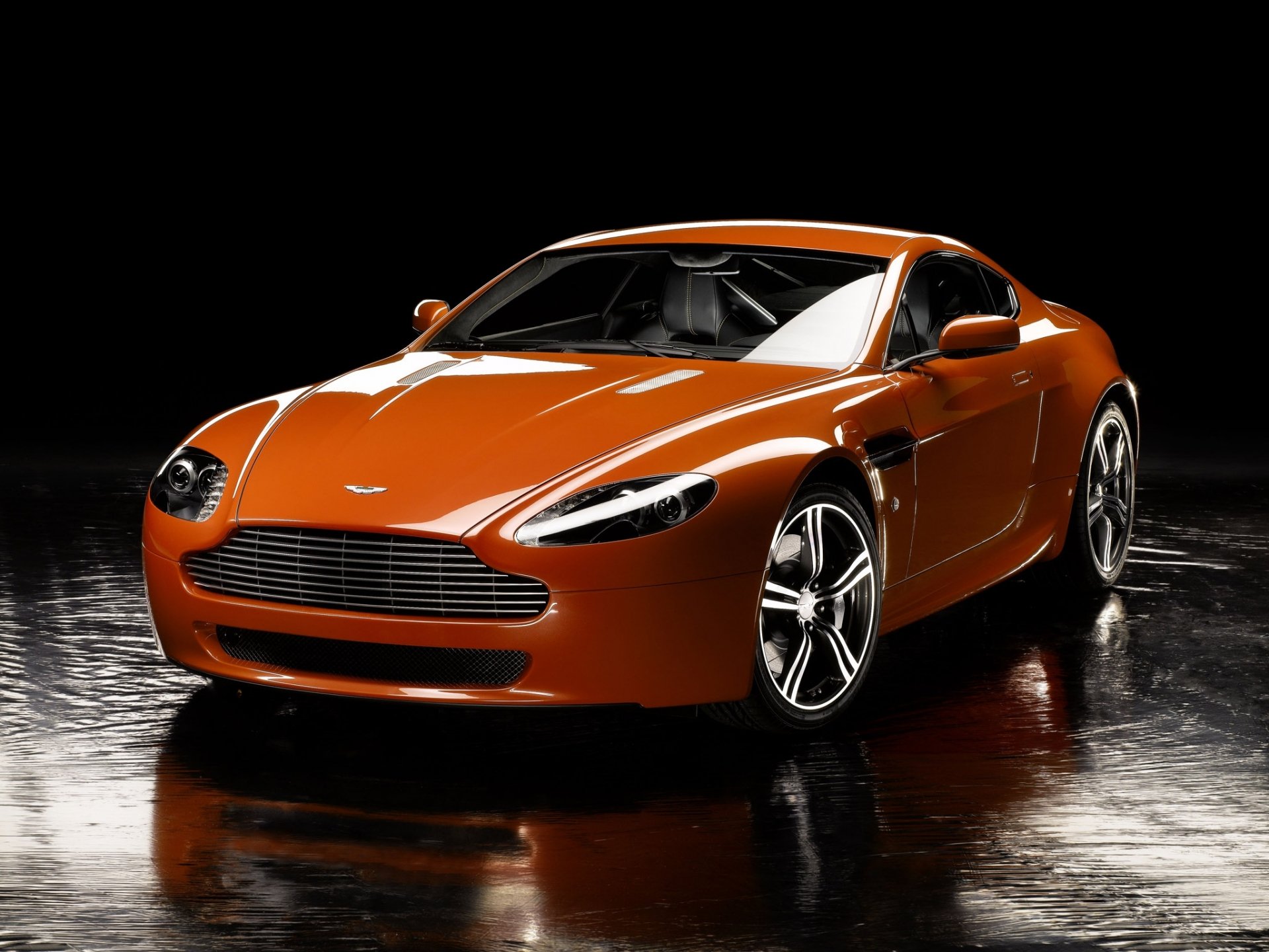 HD PC desktop wallpaper featuring an orange Aston Martin Vantage sports car against a black background.