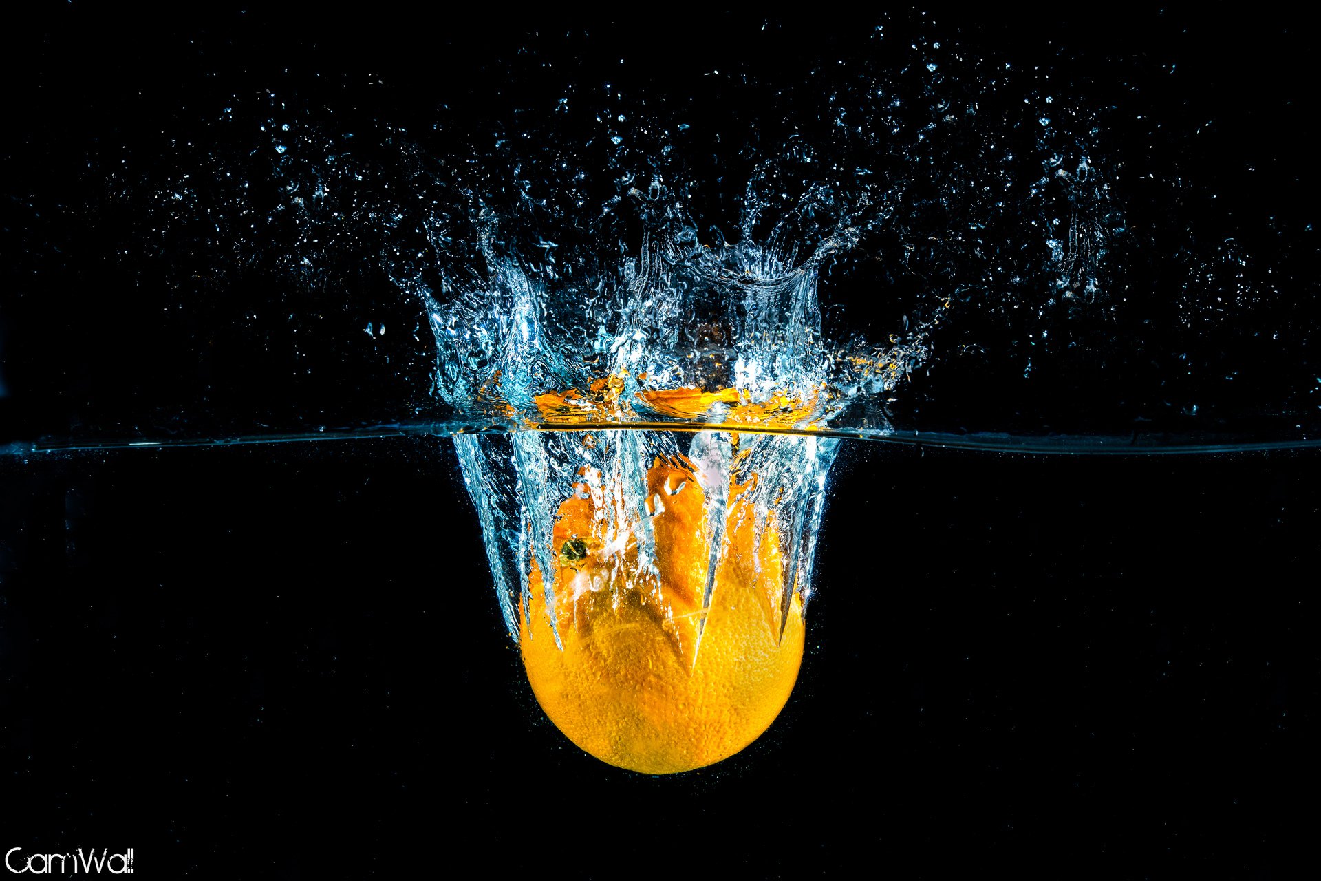 A vibrant orange fruit splashes into water, creating dynamic splashes against a dark background. This HD wallpaper captures the refreshing essence of food and color.