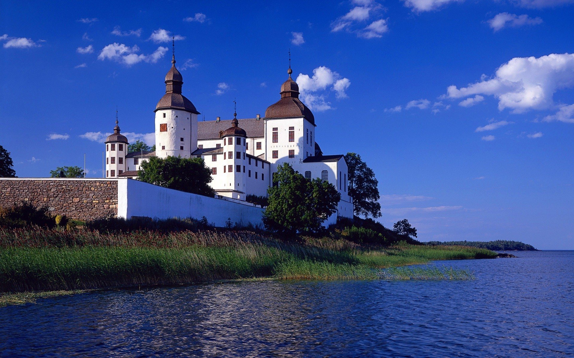 HD desktop wallpaper featuring Läckö Castle, a man-made historic castle in Sweden, set against a clear blue sky and calm waters.